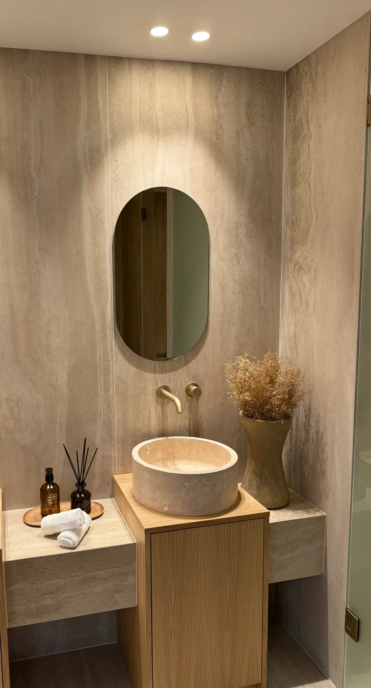 Salle d'eau habillée de travertin, vasque ronde posée sur meuble bois et miroir ovale