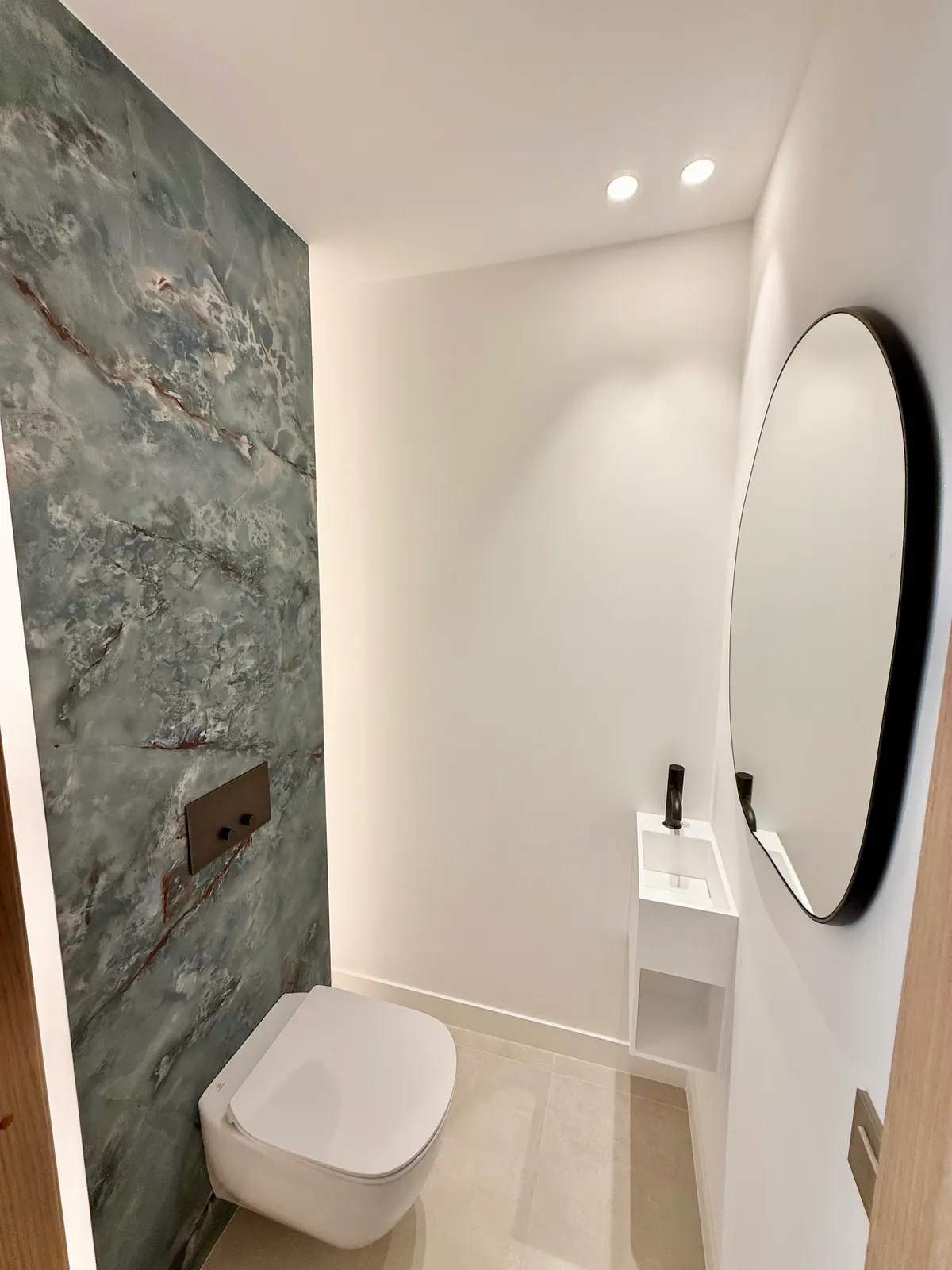 WC habillé d'un panneau de pierre verte et miroir ovale, rénovation à Cannes