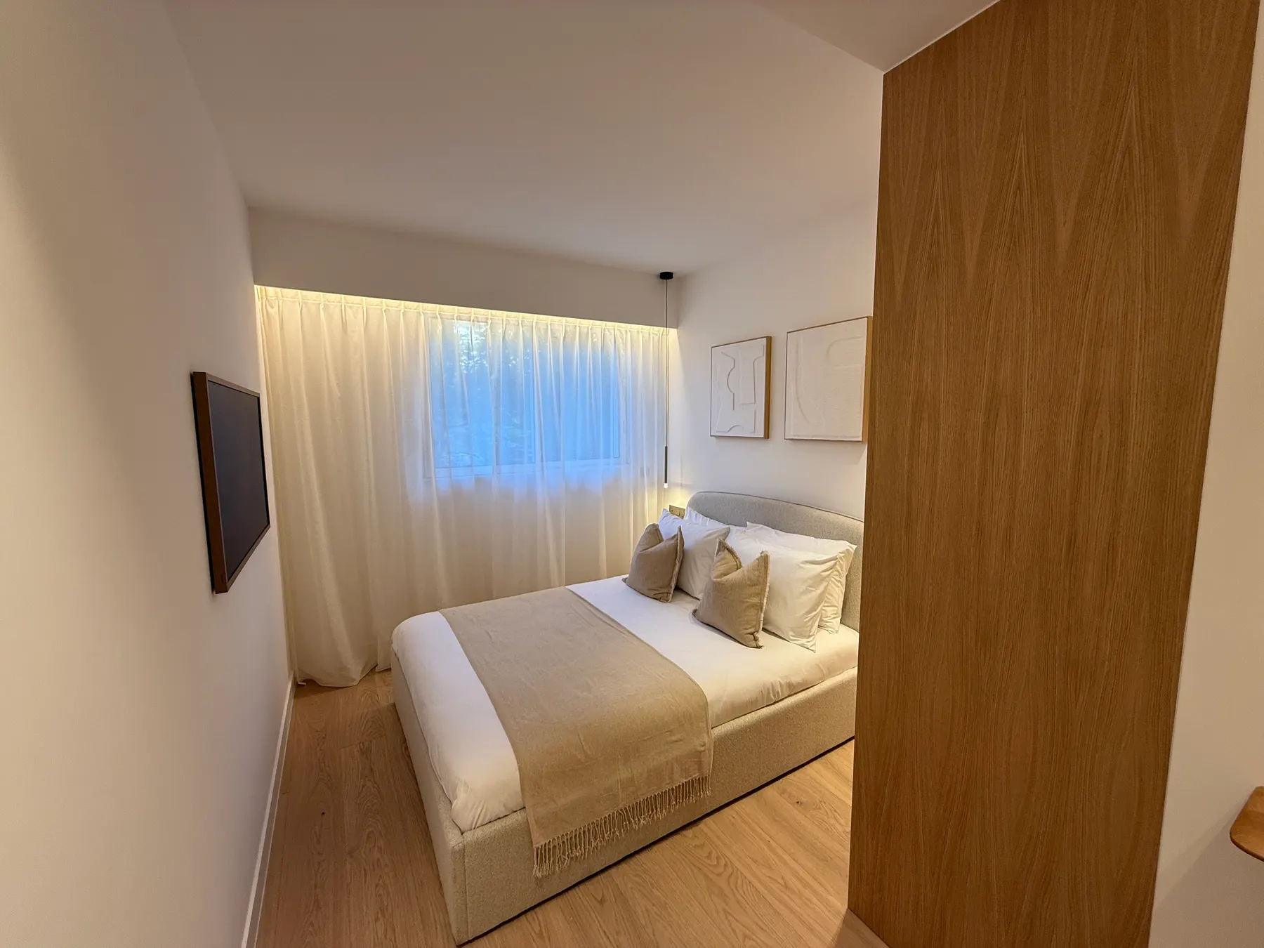 Chambre avec tête de lit en bois et voilage, appartement rénové à Cannes