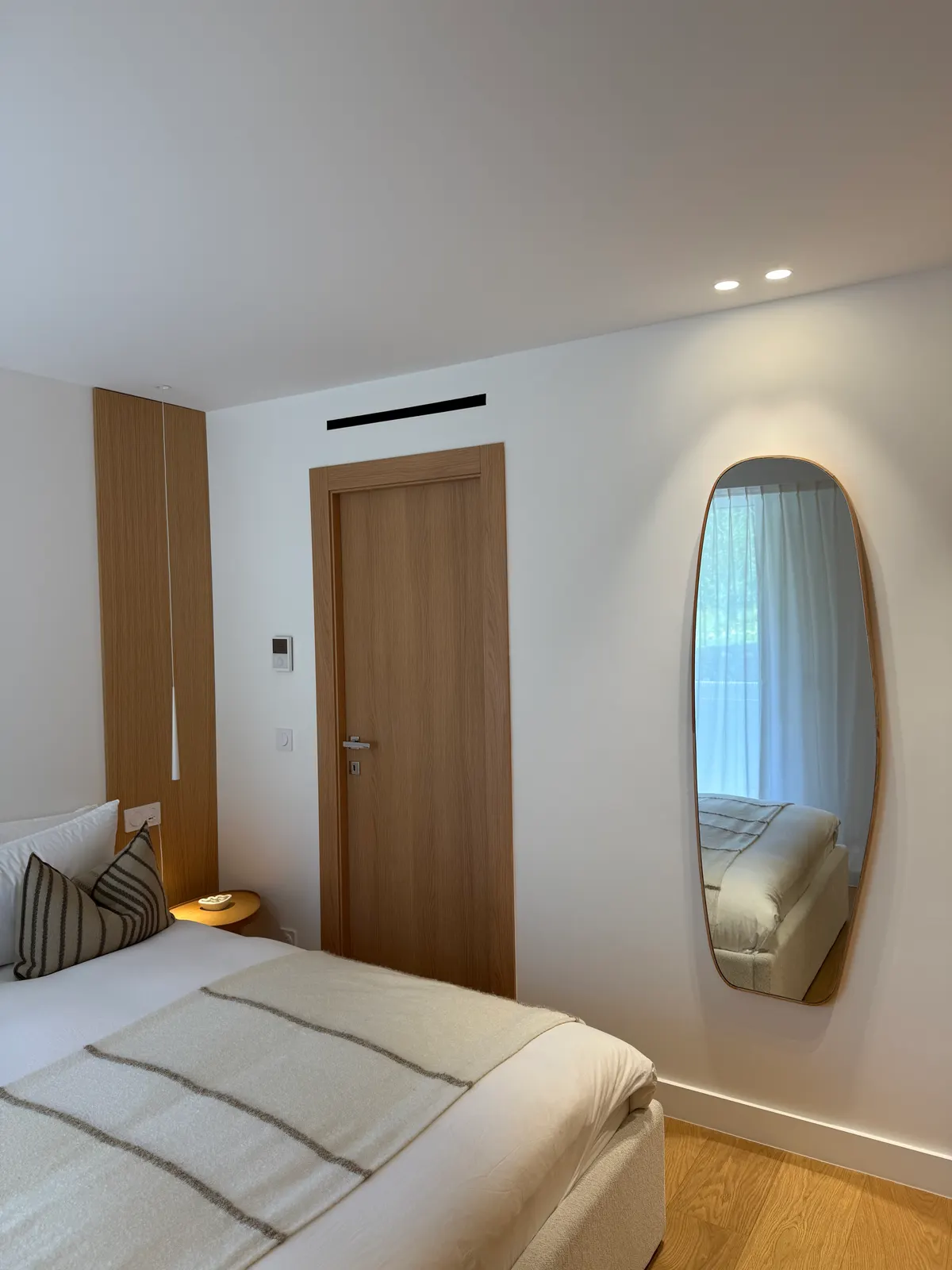 Chambre avec miroir ovale et menuiserie bois, appartement rénové à Cannes