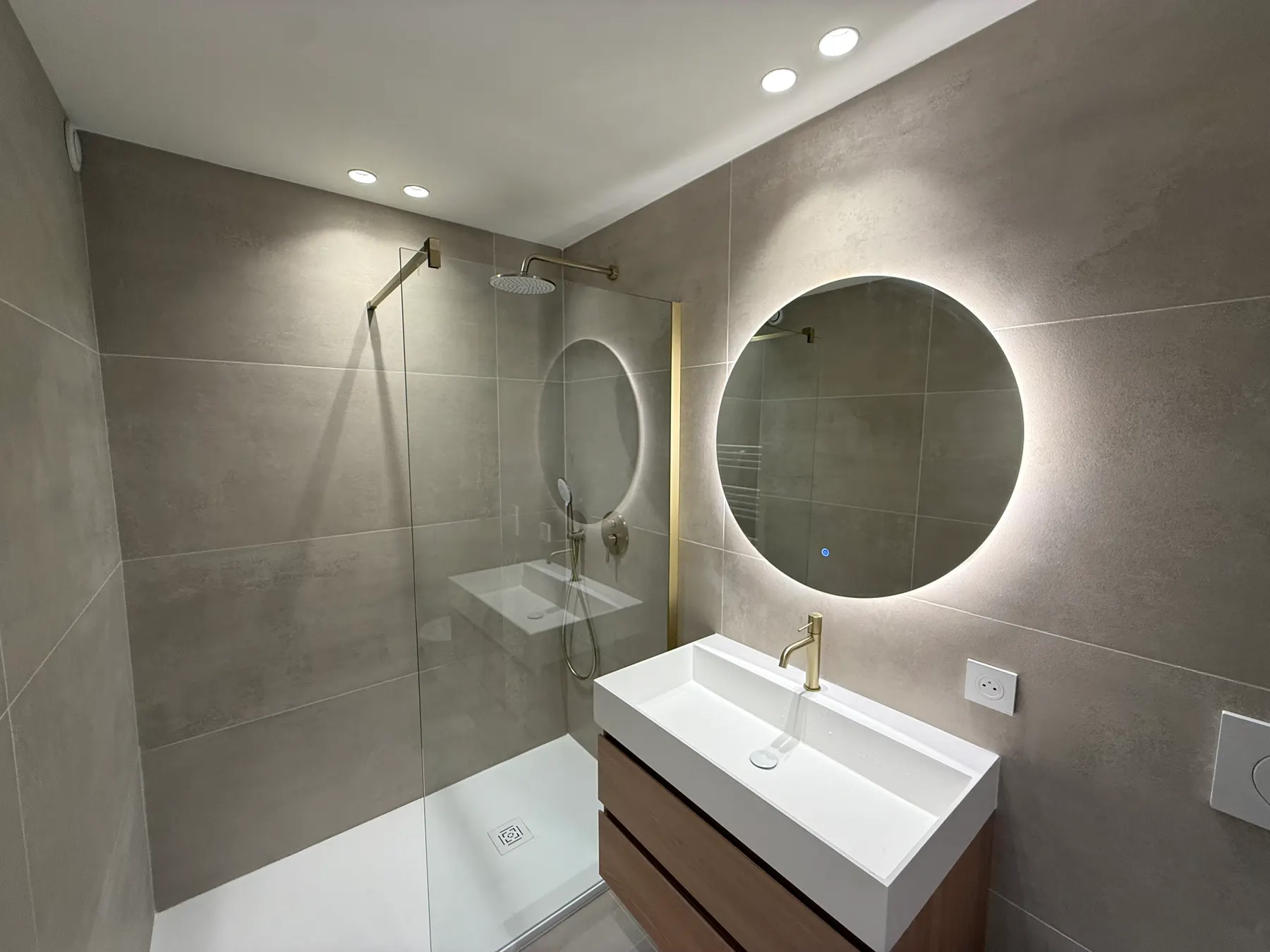 Salle de bains avec douche à l'italienne et miroir rond rétroéclairé